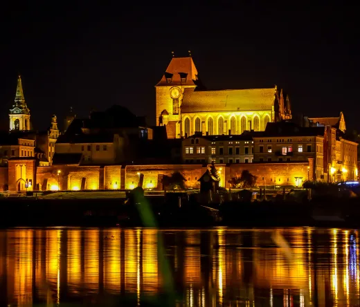 Night view of Toruń's Old Town reflected in the Vistula River.