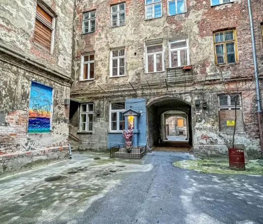Odkryj ukryty warszawska dziedziniec z zabytkowymi budynkami z cegły, sztuką uliczną i małą kapliczką.