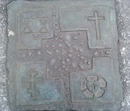Bronze plaque depicting four religious symbols: Star of David, Christian cross, Orthodox cross, and a heart with a cross.