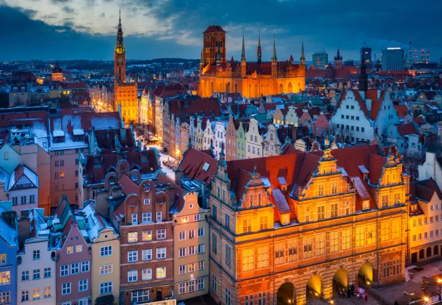 Enchanting twilight view of Gdansk's Old Town, Poland, with snow-dusted rooftops and illuminated historic buildings.