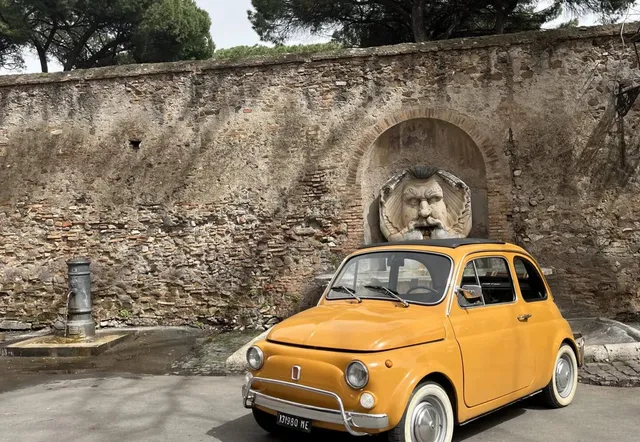 Un Fiat 500 amarillo aparcado cerca de una muralla romana con una fuente única.