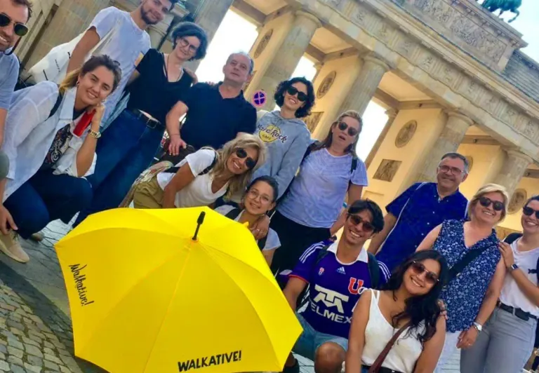 Fröhliche Touristen auf einer WALKATIVE!-Tour vor dem Brandenburger Tor in Berlin.