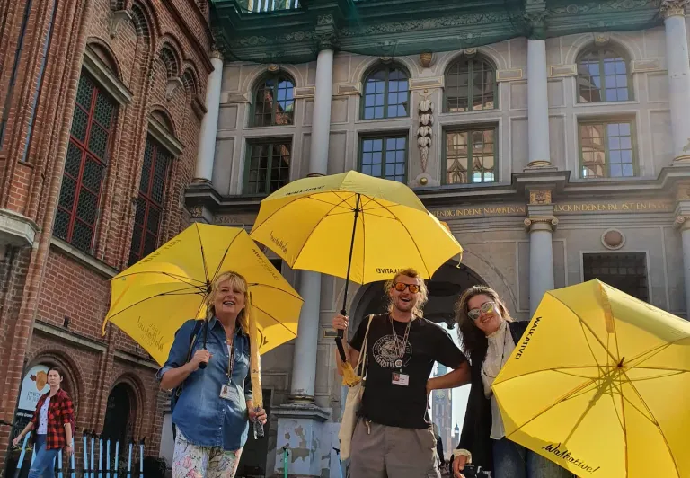 Weseli turyści na wycieczce z przewodnikiem w Gdańsku, przed Bramą Złotą.