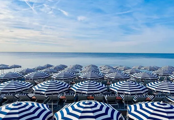 Reihen von blau-weiß gestreiften Sonnenschirmen und Liegestühlen an einem Strand in Nizza.