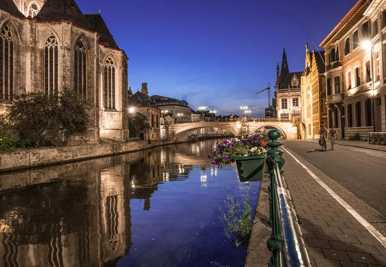 Urokliwy kanał w Gandawie nocą, odbijający historyczne budynki.