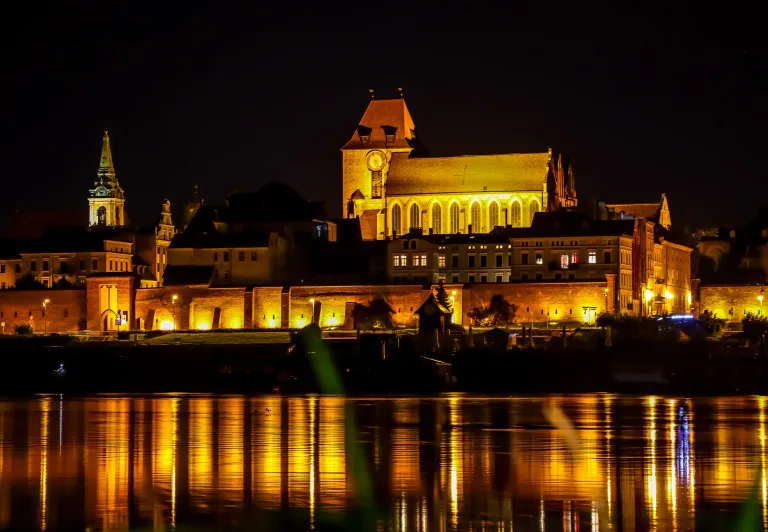 Nachtaufnahme der Altstadt von Toruń, die sich im Weichsel-Fluss spiegelt.