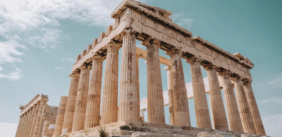Vista del templo Partenón en la Acrópolis de Atenas, mostrando columnas dóricas bajo un cielo parcialmente nublado.