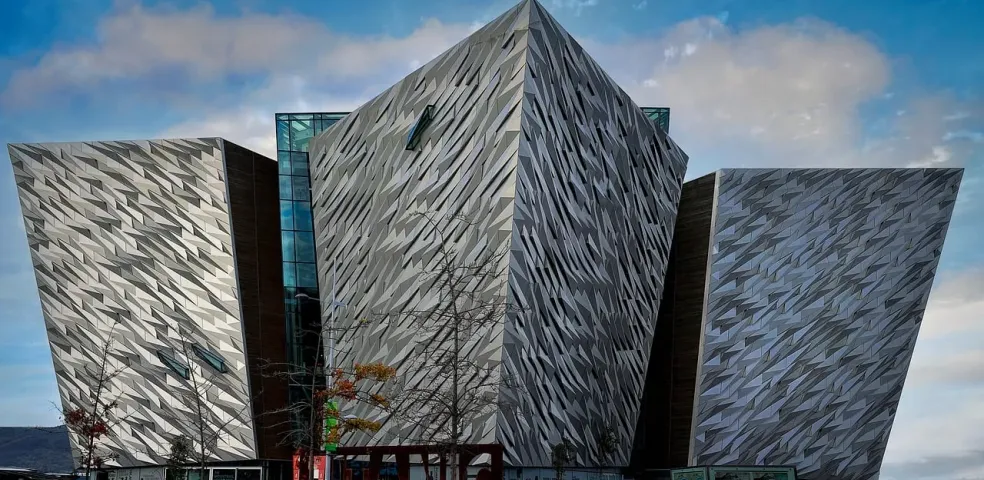 Budynek Titanic Belfast z kanciastymi, fasetowanymi srebrnymi panelami pod częściowo zachmurzonym niebem, z nagimi drzewami n