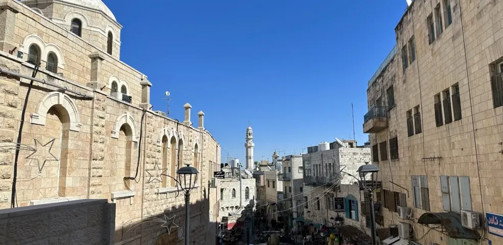 View down a stone street in Bethlehem with a large church building on the left and a distant minaret.