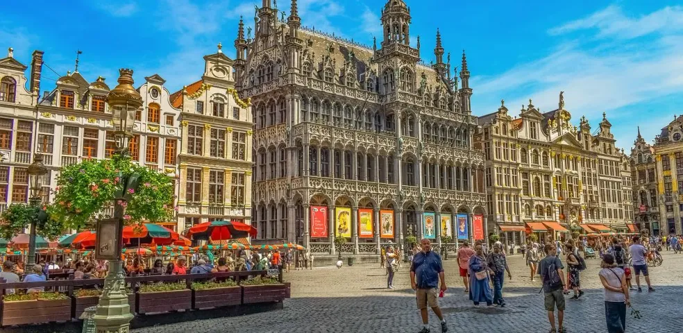 Wielki Plac w Brukseli z ozdobnymi zabytkowymi budynkami, kawiarniami na zewnątrz i ludźmi w słoneczny dzień.