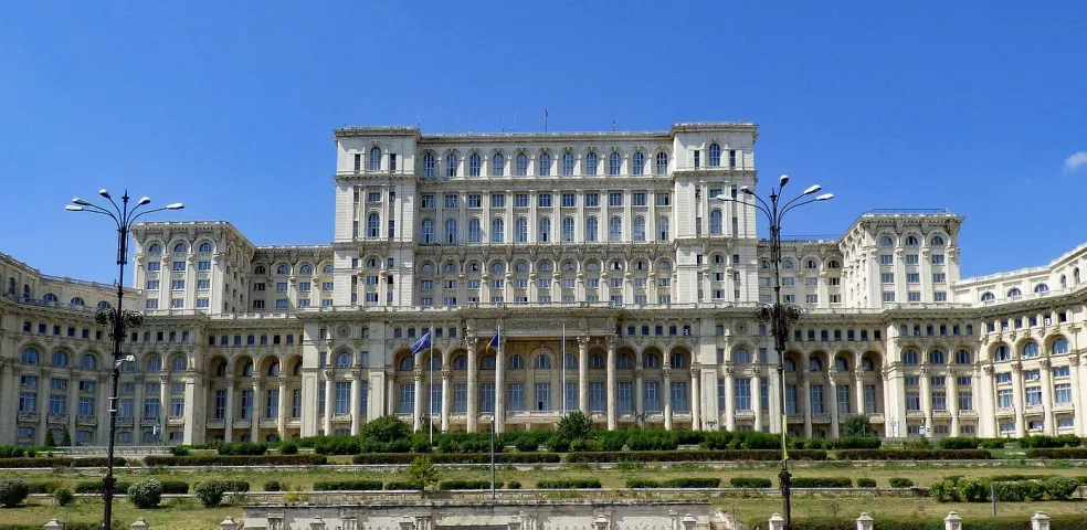 Exterior view of the Palace of the Parliament in Bucharest, Romania under a clear blue sky.