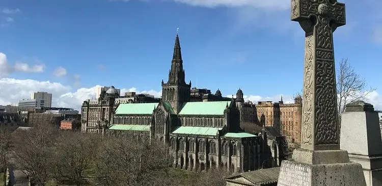 Historyczna Katedra w Glasgow z zielonym dachem i iglicą, widziana z Necropolis, z celtyckim krzyżem na pierwszym planie.