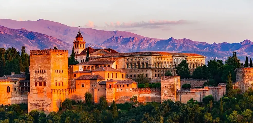 The Alhambra palace in Granada, Spain, glowing at sunset with mountains in the background.