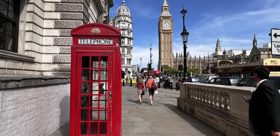 Klasyczna czerwona budka telefoniczna na londyńskim chodniku z Big Benem i Pałacem Westminsterskim w tle pod błękitnym niebem