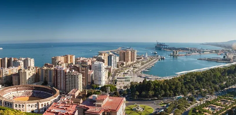 Panoramic view of Malaga, Spain, with the historic bullring, modern port, and Mediterranean Sea under clear skies.