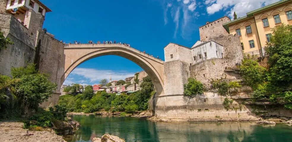 Historische Stari Most Brücke in Mostar, Bosnien und Herzegowina, über einem grünen Fluss, mit alten Steingebäuden und Uferve