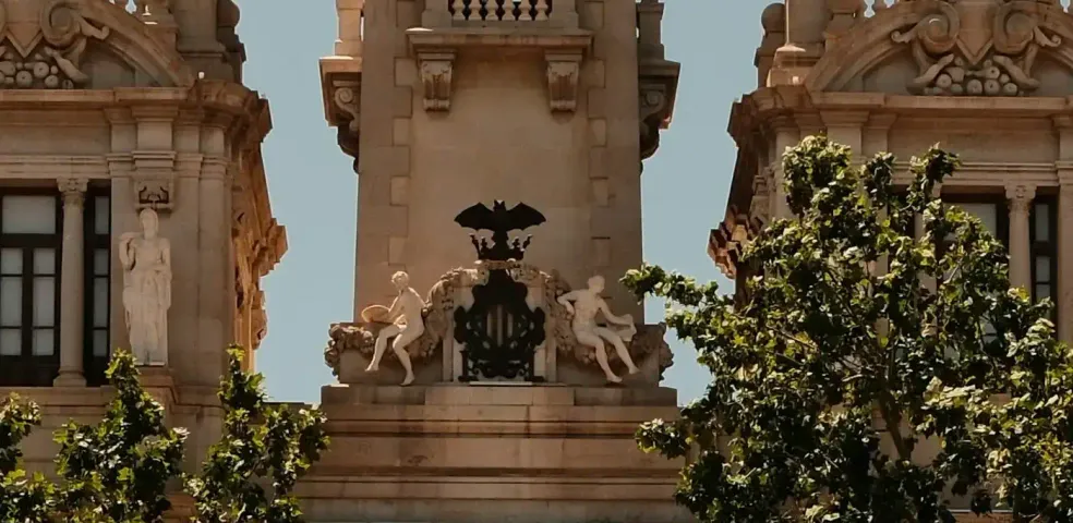 Full view of Valencia City Hall with central clock tower, flanked by domes, in a large, sunny square.