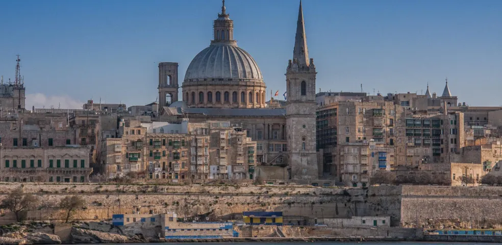 Valletta skyline with Grand Harbour, featuring a large cathedral dome and spire rising above historic buildings.