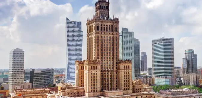 Aerial view of the Palace of Culture and Science and modern skyscrapers under a partly cloudy sky in Warsaw.