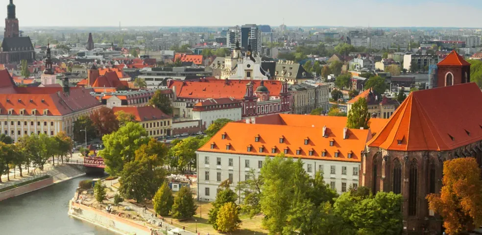 Panoramic aerial view of Wroclaw cityscape with the Odra River, historic buildings with red roofs, church towers, and lush gr