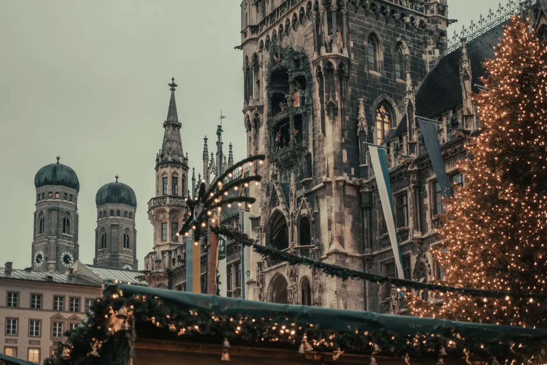 Münchner Neues Rathaus und Frauenkirche hinter beleuchtetem Weihnachtsbaum und Marktstand.