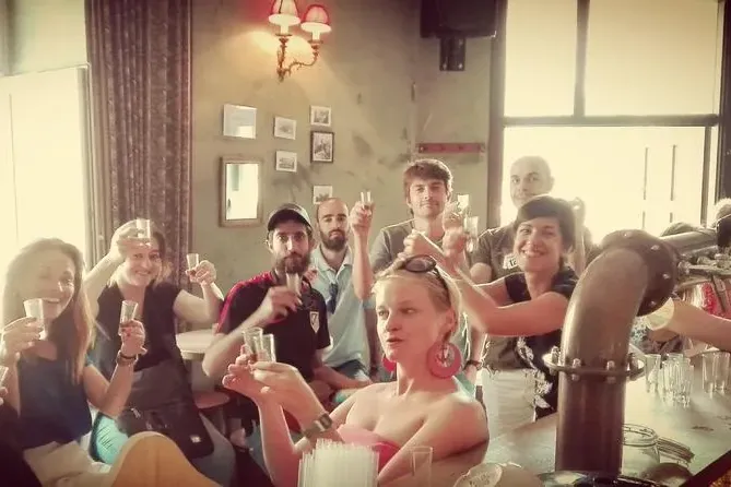 Grupo de personas diversas sonriendo y levantando pequeños vasos, posiblemente para una degustación, en una barra de bar. ...