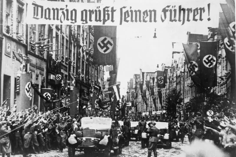 Schwarz-weißes Historienbild einer Straße in Danzig (Gdańsk) während einer NS-Parade mit Menschenmassen, Fahrzeugen, Haken...