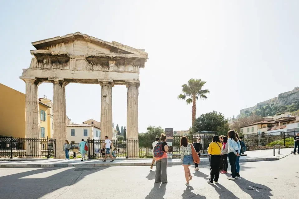 Antikes Tor der Athena Archegetis an der Römischen Agora in Athen, mit Touristen und Palme an einem Sonnentag.