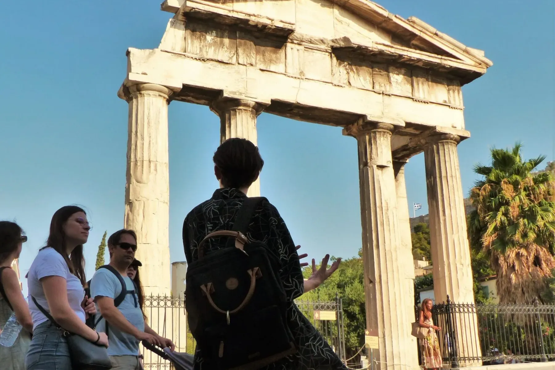 Reisegruppe betrachtet den antiken Hadriansbogen in Athen, ein großes Steingebäude mit Säulen unter blauem Himmel.