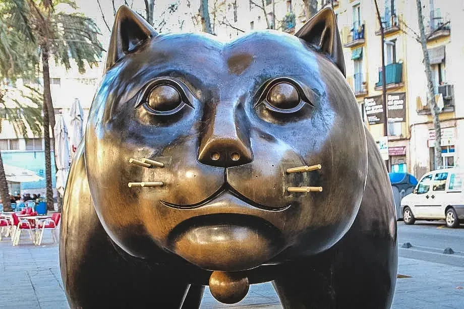 Große Bronzeskulptur einer dicken Katze mit runden Augen und Messing-Schnurrhaaren auf einer Palmenallee in Barcelona.