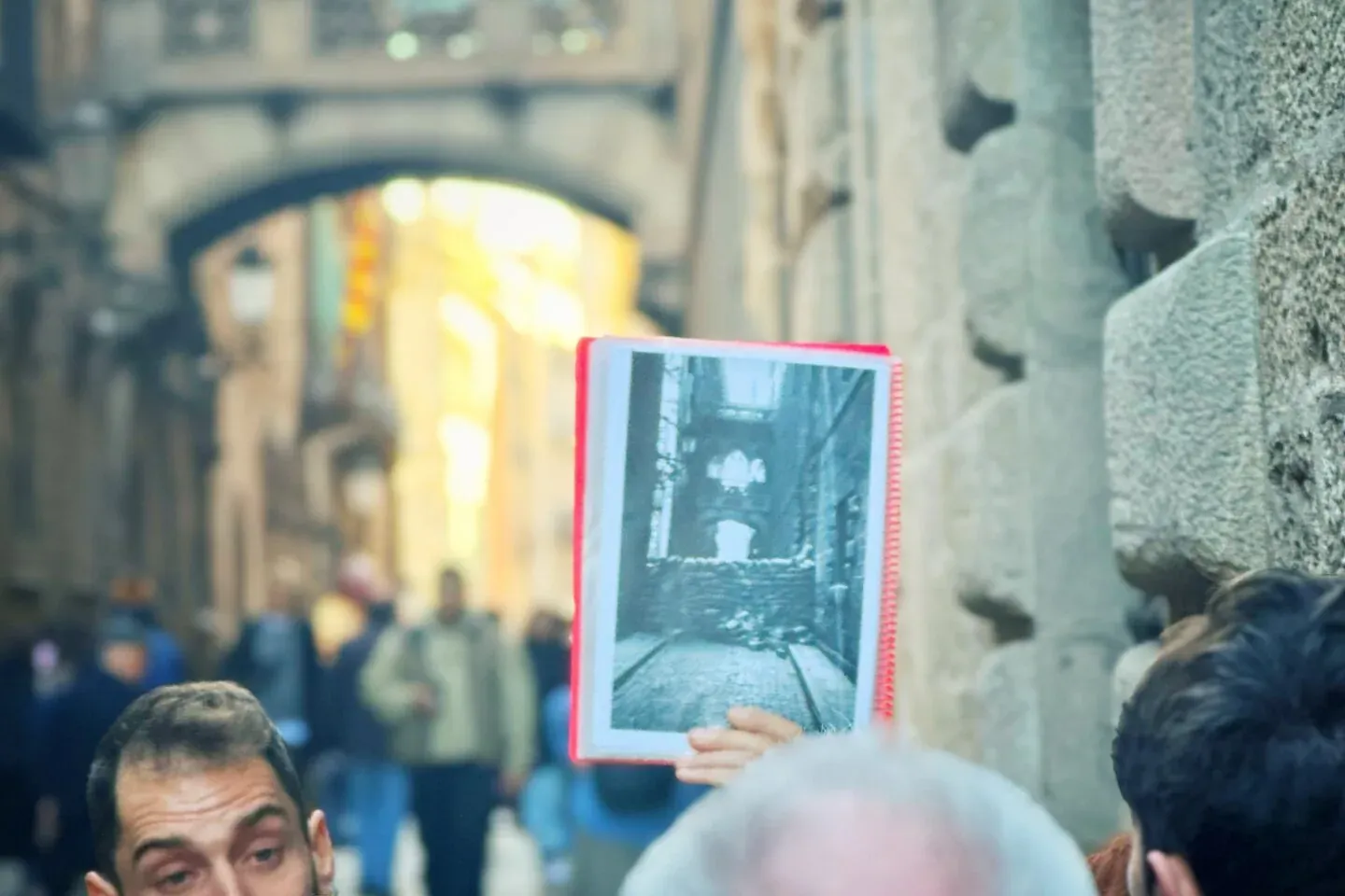 Männlicher Reiseführer zeigt Touristen ein altes Schwarz-Weiß-Foto einer Straße, mit historischer Architektur und einer Bo...