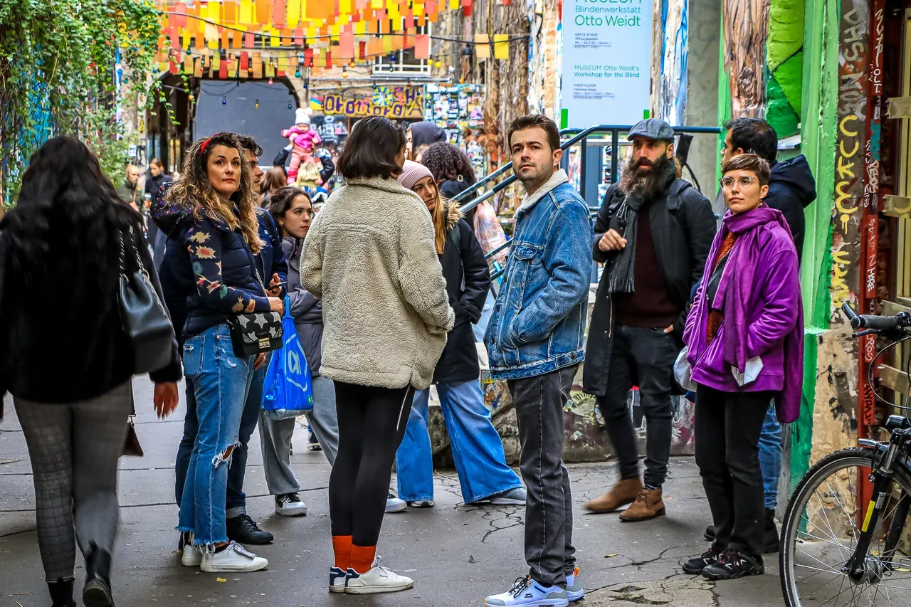 Gruppe von Menschen in einer schmalen, kunstvollen Gasse mit Graffiti-Wänden und bunten Wimpeln. Ein Museumsschild ist sic...