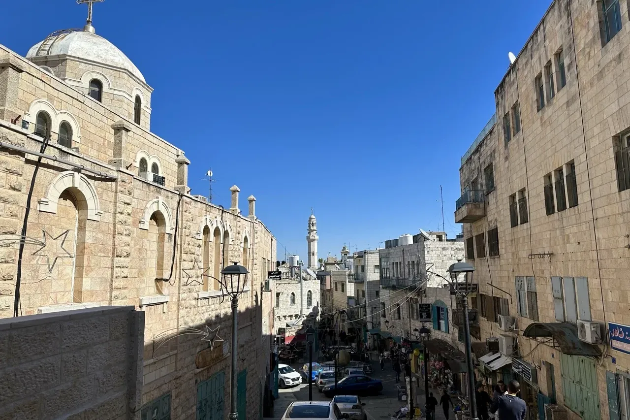 Vista de una calle de piedra en Belén con un gran edificio de iglesia a la izquierda y un minarete distante.