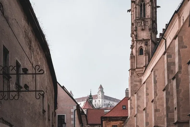Calle adoquinada que conduce a la torre de la Catedral de San Martín y al Castillo de Bratislava en un día nublado.