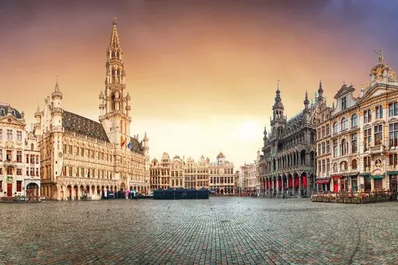 Vista panorámica de la Grand Place de Bruselas con elaborados gremios y el Ayuntamiento bajo un cielo dramático y colorido.