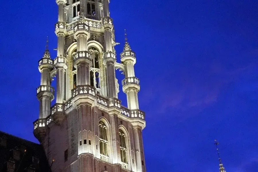 Torre gótica iluminada y fachada del Ayuntamiento de Bruselas bajo un cielo nocturno azul oscuro, con banderas de Bélgica ...