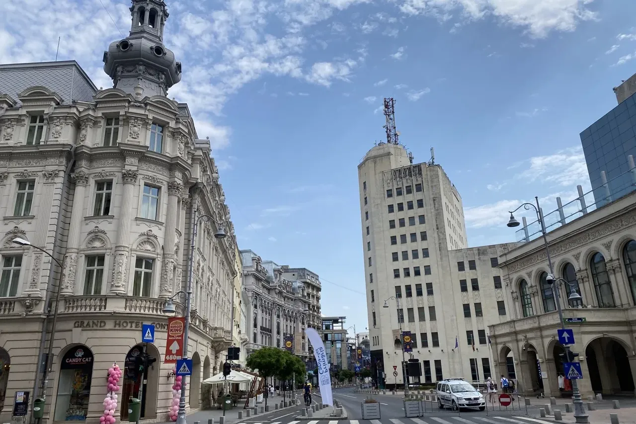 Vista de una calle de Bucarest con el ornamentado Grand Hotel Continental y el alto Palatul Telefoanelor bajo un cielo nub...
