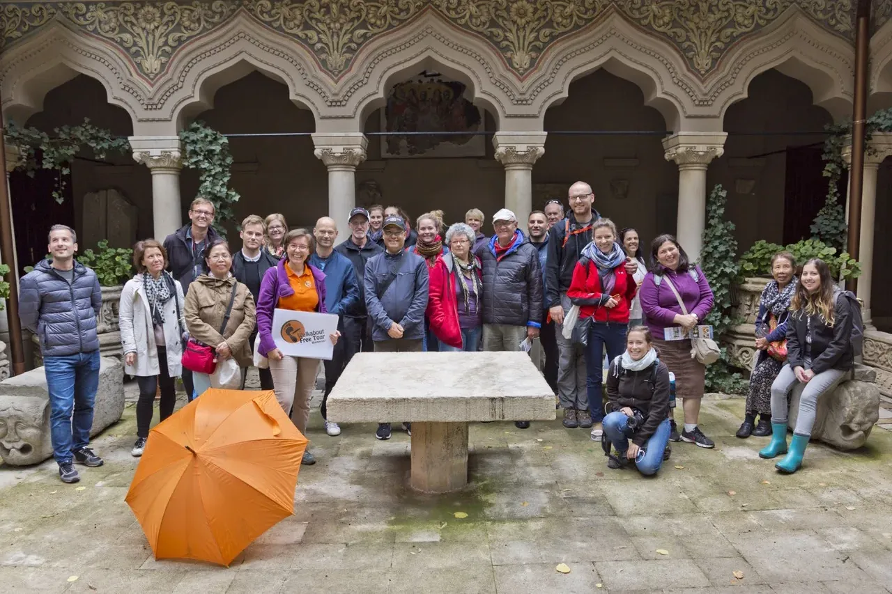 Un grupo de turistas con guía en el ornamentado patio de arcos del Monasterio de Stavropoleos en Bucarest, con un paraguas...