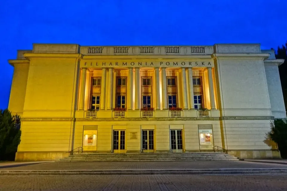 Beleuchtetes klassizistisches Gebäude der Pommerschen Philharmonie in Bydgoszcz bei Nacht, mit Säulen und Treppen unter bl...
