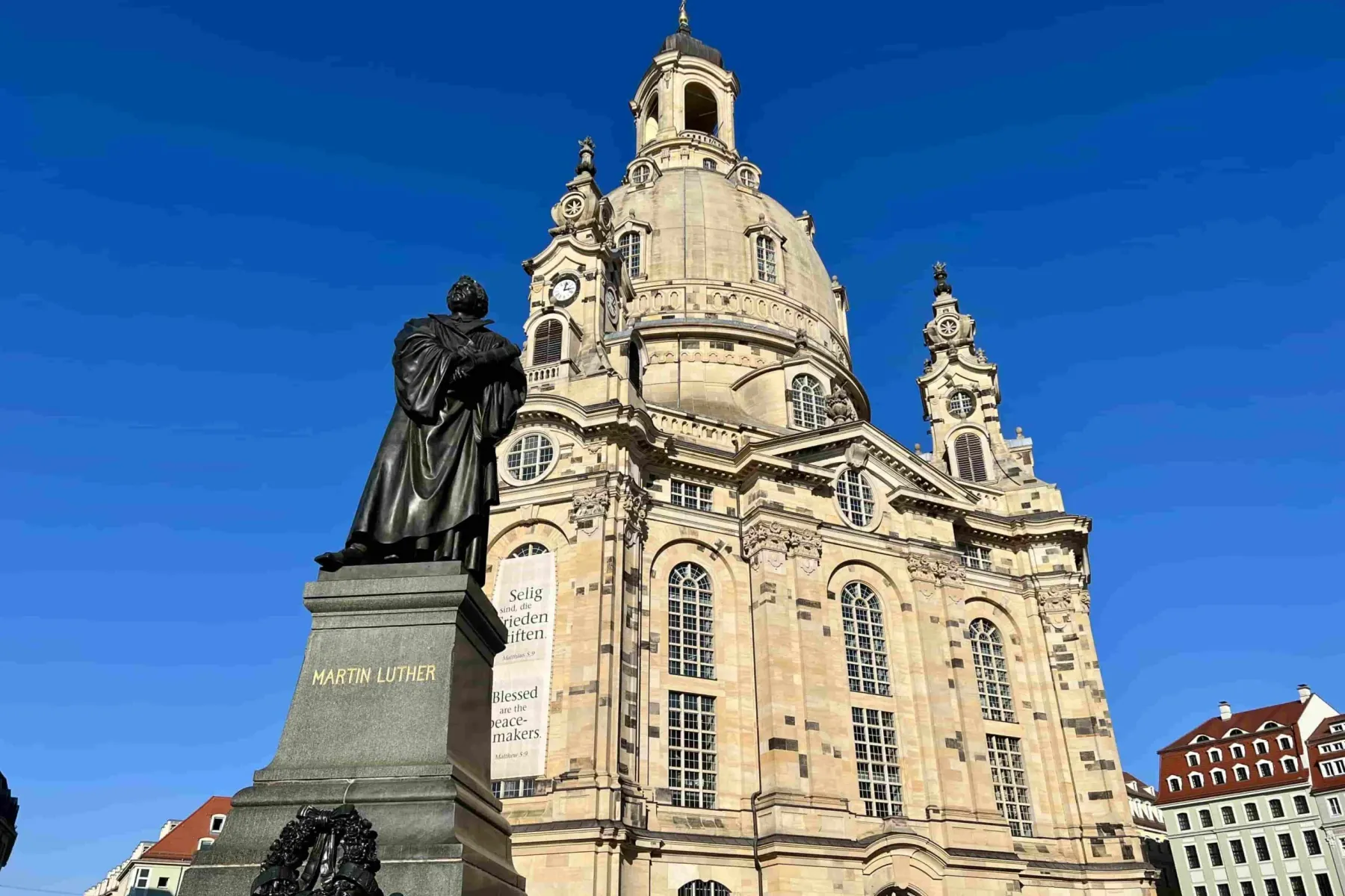 The Martin Luther statue in front of Dresden Frauenkirche under a clear blue sky, showing its dome and baroque facade.