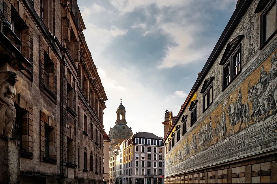 Calle adoquinada en Dresde hacia la cúpula de la Frauenkirche, flanqueada por edificios antiguos y el mural del Fürstenzug...