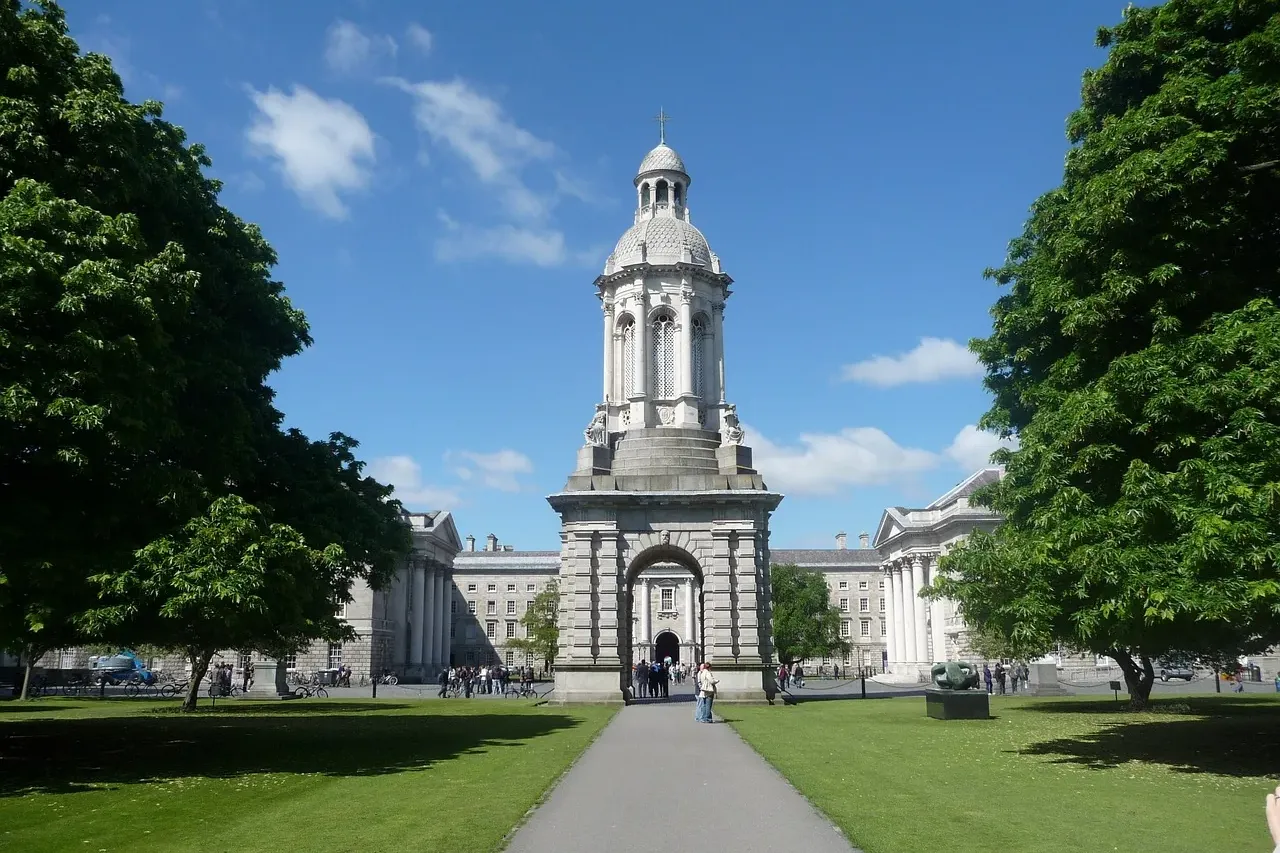 Biała kamienna dzwonnica Campanile Trinity College w Dublinie, otoczona zielonymi trawnikami i zabytkowymi budynkami pod b...