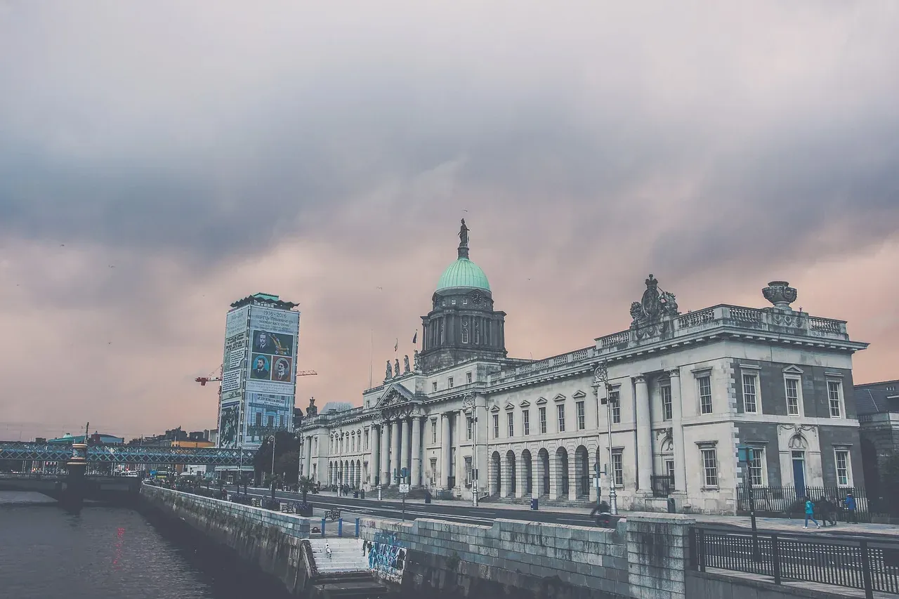 Gmach Celny w Dublinie, neoklasyczny budynek z zieloną kopułą, nad rzeką Liffey pod zachmurzonym niebem.