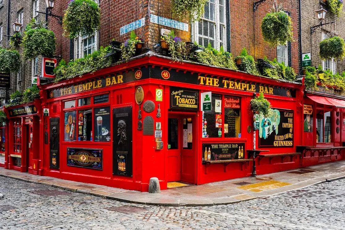 Czerwony budynek pubu "The Temple Bar" na rogu brukowanej ulicy, z wiszącymi roślinami i ceglanymi budynkami.
