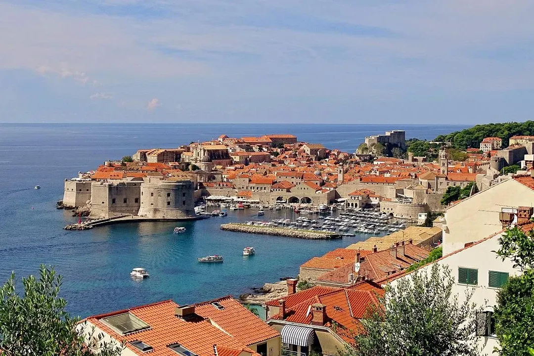 Vista elevada del Casco Antiguo de Dubrovnik, con tejados rojos, murallas medievales, un puerto con barcos y el mar Adriát...