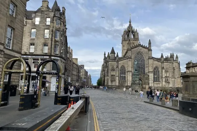 St Giles' Cathedral mit Kronenturm, eine Kopfsteinpflasterstraße mit historischen Steingebäuden und Passanten unter bewölk...