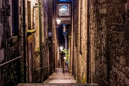 Enge Kopfsteinpflastergasse in Edinburgh bei Nacht, gesäumt von hohen Steingebäuden und beleuchtet von Straßenlaternen.