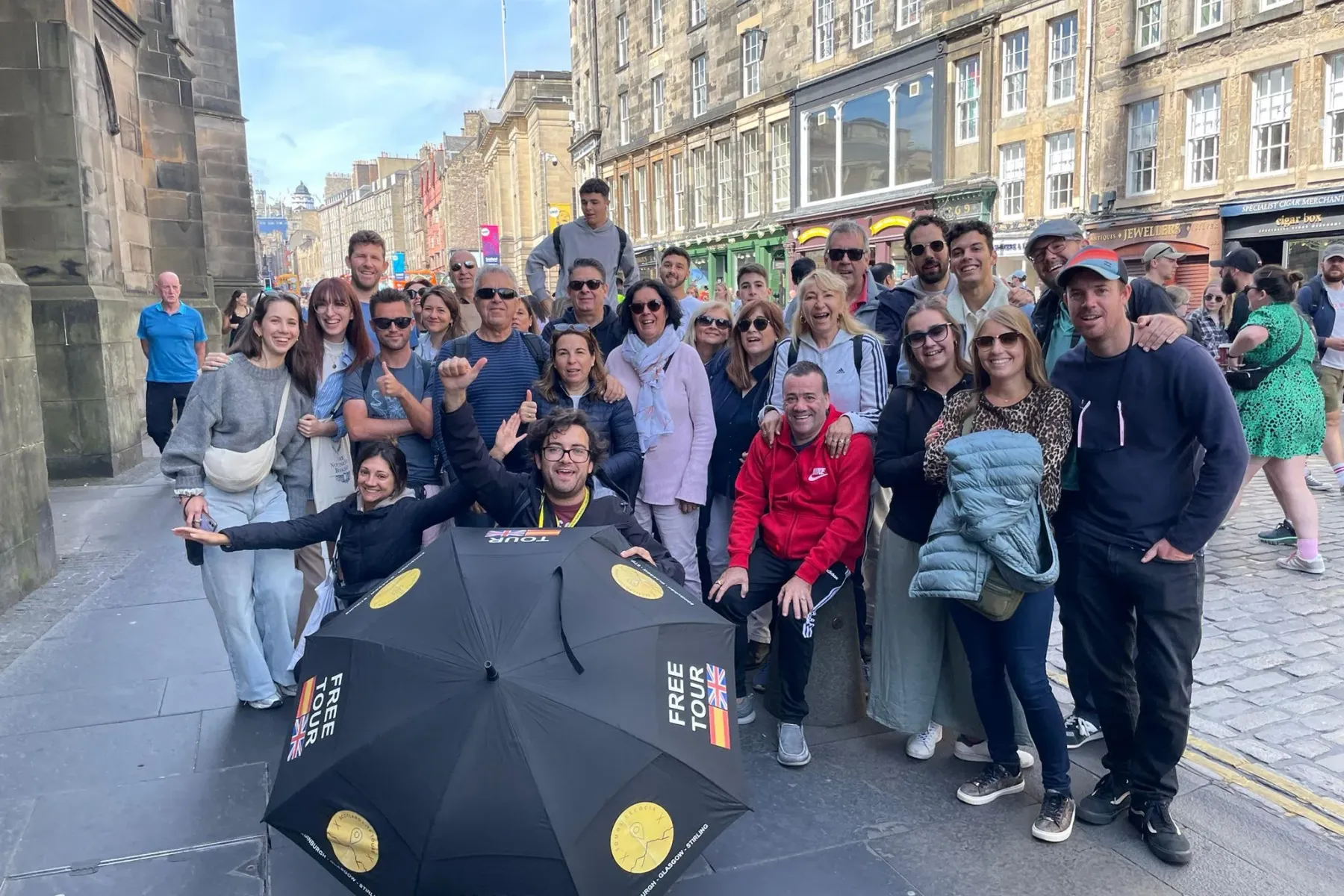 Eine gemischte Gruppe lächelnder Touristen und ihr Reiseführer mit einem 'Free Tour'-Regenschirm auf einer Kopfsteinpflast...
