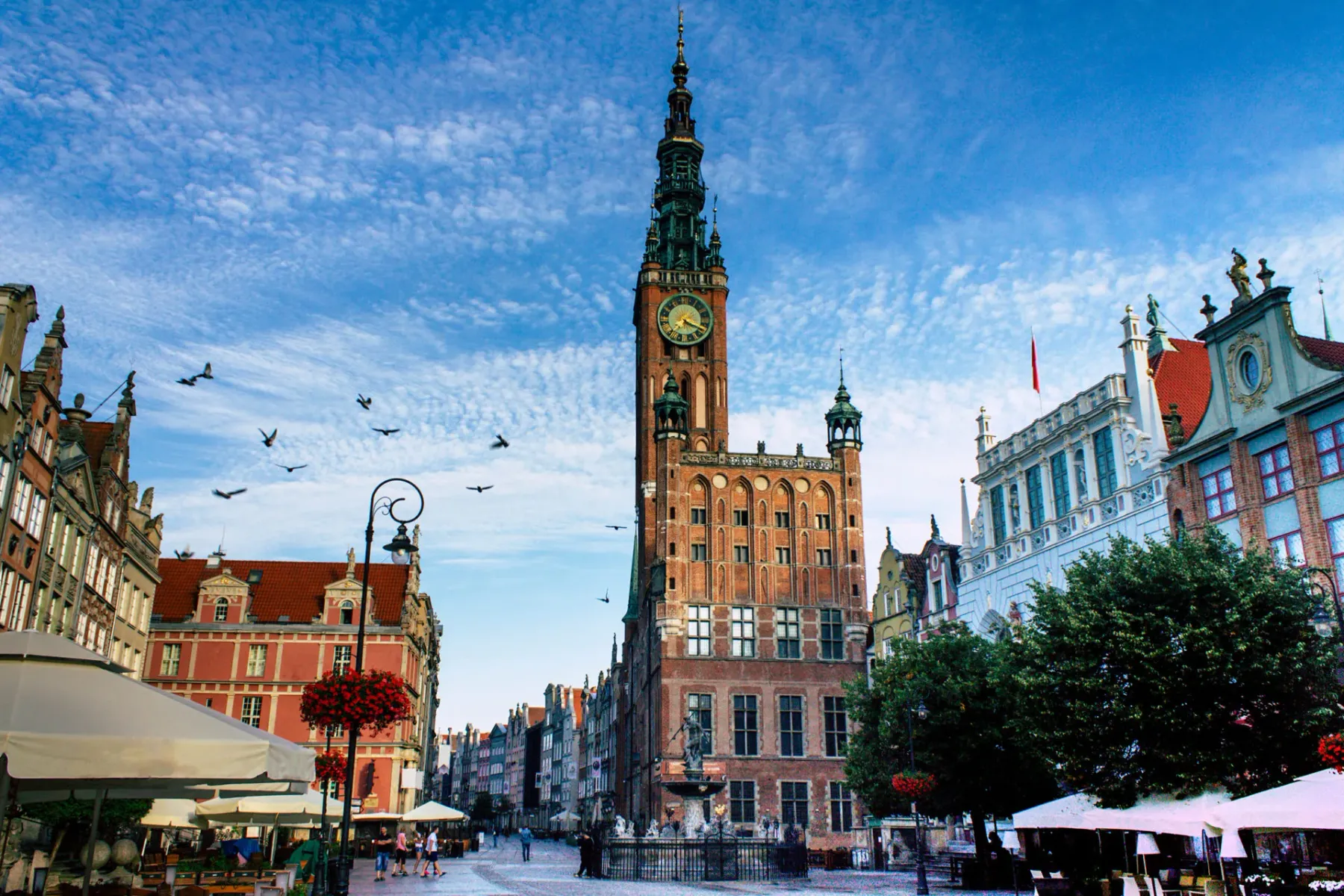 Hauptstädtisches Rathaus in Danzig mit hohem Turm und Uhr, umgeben von historischen Gebäuden und Spaziergängern.