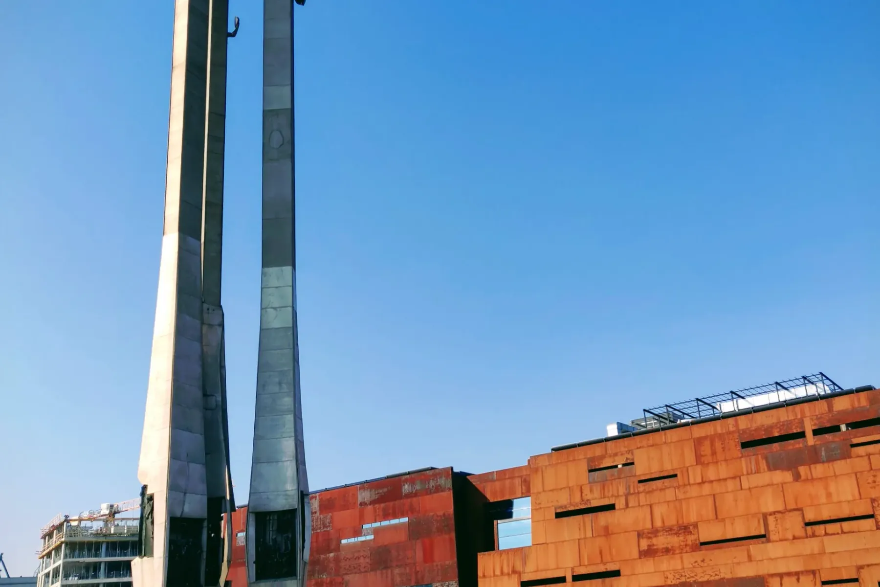 Denkmal Gefallene Werftarbeiter 1970, Danzig, drei Kreuze und Anker, neben rostbraunem Gebäude unter blauem Himmel.